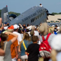 The crowd looks to the sky in unison at the F18 above them while the JU-52 rests.