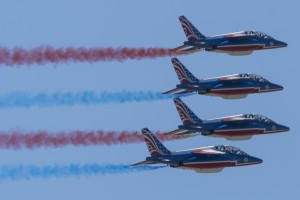 The outside wingmen and solos pass in a stacked formation trailing red and blue smoke. 