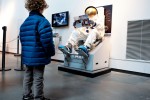 A child watches the stand-alone space shuttle potty exhibit, manned by Museum of Flight webmaster Layne Benofsky thumbing through a magazine in a spacesuit. (Photo by Jeremy Dwyer-Lindgren/NYCAviation)