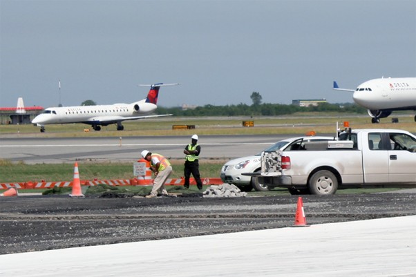Construction personnel are seen completing work on the north side of the Bay Runway as two arriving aircraft taxi to the terminal