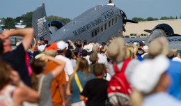 The crowd looks to the sky in unison at the F18 above them while the JU-52 rests.